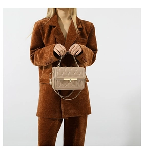 Detail of a quilted beige tote bag with gold buckle on a model in a brown suit