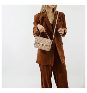 Quilted beige square handbag with gold metal detail shown on a corduroy blazer