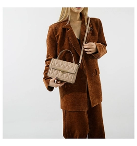 Detail of beige quilted leather handbag with metallic lock and curved handle on a model