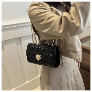 Détail du sac à bandoulière matelassé noir avec boucle cœur dorée et bandoulière chaîne