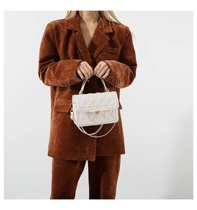 White quilted crossbody bag with gold lock buckle worn with brown corduroy outfit