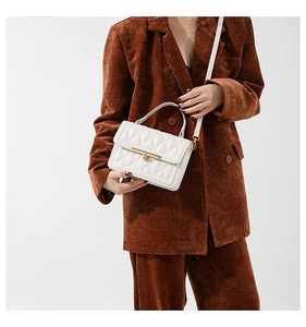 Close-up of white quilted crossbody bag with gold buckle on brown corduroy blazer