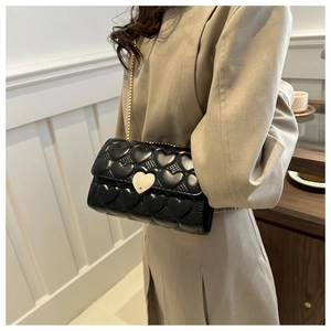 Détail du sac en cuir noir surpiqué en cœur avec chaîne dorée et boucle cœur en métal