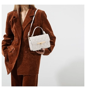 Detail of white quilted crossbody bag with gold lock shown on brown corduroy suit