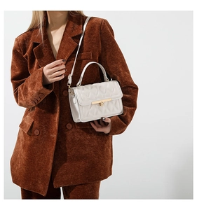 Close-up of white quilted handbag with gold lock on brown corduroy blazer outfit
