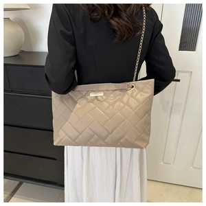 Detail der beigen Stepptasche mit goldener Kette und Metallplakette am Modell