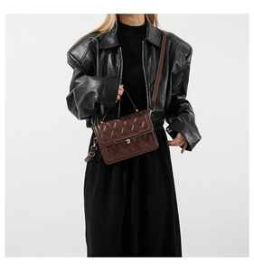 Close-up of brown quilted leather handbag with gold metal lock worn by fashion model