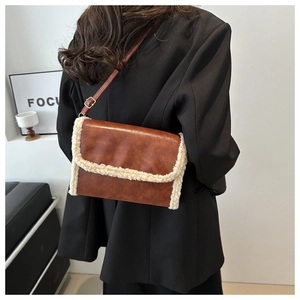 Detail of brown PU leather crossbody bag with white faux shearling trim on black blazer