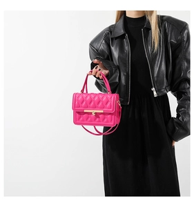 Close-up of a pink quilted crossbody bag with gold metal handle on a black leather outfit