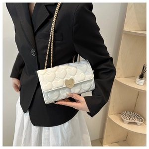 Détail du sac bandoulière blanc avec matelassage en cœur et boucle dorée en forme de cœur