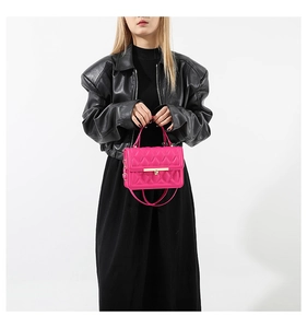 Model wearing a rose red quilted crossbody bag with gold buckle and chain strap