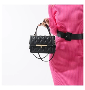 Detail of black quilted crossbody bag with golden metal buckle and leather handle