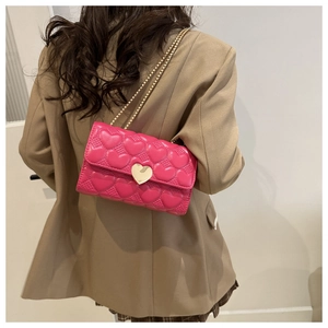 Sac bandoulière rose fuchsia avec matelassage cœur et chaîne dorée porté par un mannequin