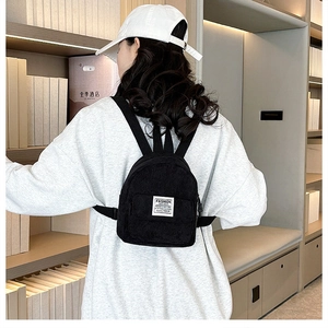 Detailopname van een zwarte corduroy mini-rugzak met een wit merklabel gedragen door een model