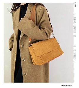 Detail of ginger suede crossbody bag with wide strap on a brown coat model