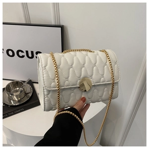 Détail d'un sac à bandoulière matelassé blanc avec texture cœur et chaîne dorée
