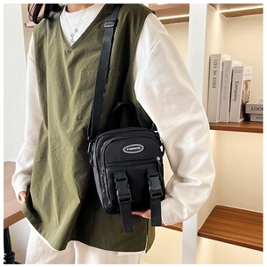Detail van zwarte nylon mini crossbodytas met modieuze patch en dubbele gespsluiting