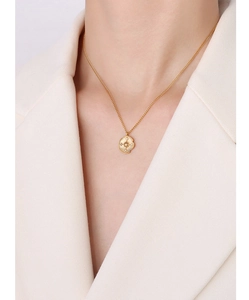 Close-up of a gold compass pendant necklace worn over a stylish cream blazer