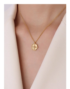 Detail of a gold compass star pendant with zircon inlay on a textured disc necklace
