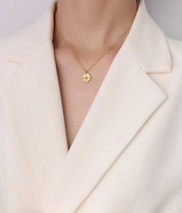 Close-up of a gold compass pendant necklace with zircon star detail worn by a model