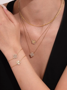 Détail de colliers dorés superposés et de pendentifs trèfle avec zircons brillants
