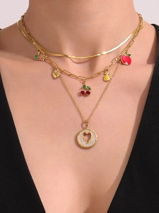 Primer plano de collar de tres capas en oro de 18K con dijes de frutas y colgante de corazón