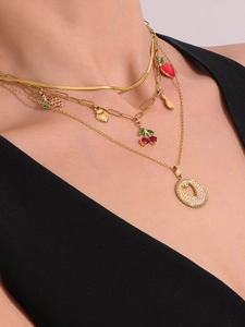 Detalle de collar de capas de oro 18k con dijes de frutas y colgante de circonita