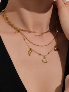 Dettaglio di collane d'oro a strati con ciondoli a forma di delfino e balena su modella