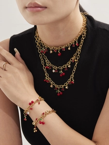 Détail de colliers avec pendentif cerise rouge et bracelet perlé porté sur modèle