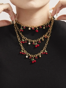 Gros plan du collier cerise doré à trois rangs avec émail rouge et zircon sur pull noir