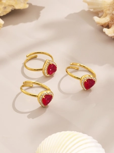 Detail of three gold rings featuring red heart gemstones with zircon halo settings