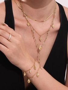 Dettaglio dei ciondoli a cuore e croce dorati su collana e bracciale a più strati