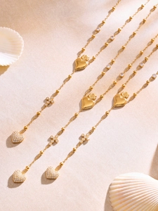Dettaglio di collane placcate in oro con cuori in zircone e croci su sfondo di sabbia