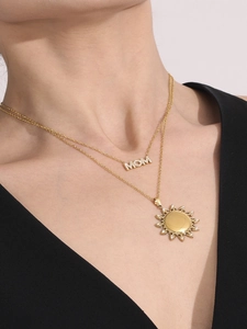 Detail van gelaagde gouden ketting met MOM-letters en zonnehanger met zirkonia