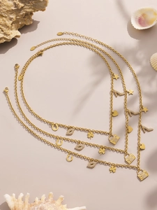 Detail of layered gold stainless steel necklaces with heart and star charms on sandy beach