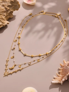 Dettaglio delle collane a strati in oro 18K con ciondoli a stella, luna e perle su pietra