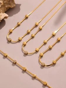 Dettaglio macro di catene a serpente dorate con pendenti a fiore e zirconi micro-pavé