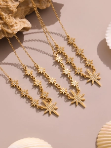 Dettaglio di collane a stella in oro 18K con zirconi su uno sfondo beige naturale