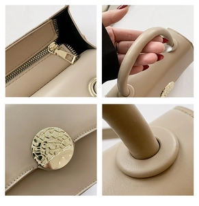 Detail view of smooth metal zipper, round handle and gold textured buckle on beige bag