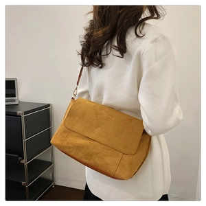 Side view of large mustard yellow faux suede crossbody bag worn by a model in a studio