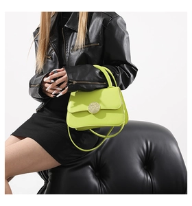 Neon lime green crossbody bag with gold circular metal buckle held by model in black