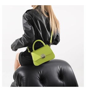 Detail of neon green crossbody bag with a circular hollow metal clasp on black leather