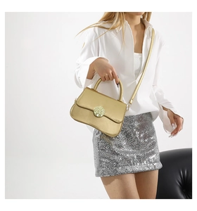 Golden matte crossbody bag with handle shown in a stylish urban outfit setting