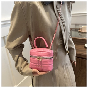 Détail d'un sac seau matelassé rose avec chaîne dorée tenu par un mannequin au café