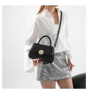 Detail of a chic black leather crossbody bag with a hammered gold metal clasp on the flap
