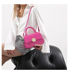 Model wearing a bright pink crossbody bag with round gold buckle on white background