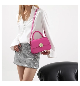 Detailed view of rose red leather crossbody bag with large gold buckle and strap