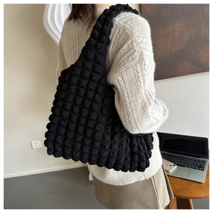 Detailed view of black popcorn texture tote bag with wide shoulder strap worn by a model
