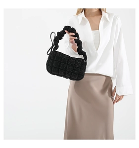 Detail of black quilted puffer bag featuring a ruffe handle and side bow accent