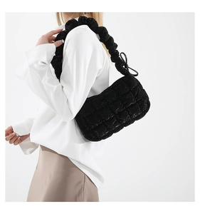 Side view of black quilted cloud shoulder bag with ruffled strap worn by model